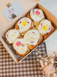 Rollitos de canela y manzana jugosa de 8 cm aproximadamente cada uno. Con frosting de queso crema y flores comestibles en su parte superior.